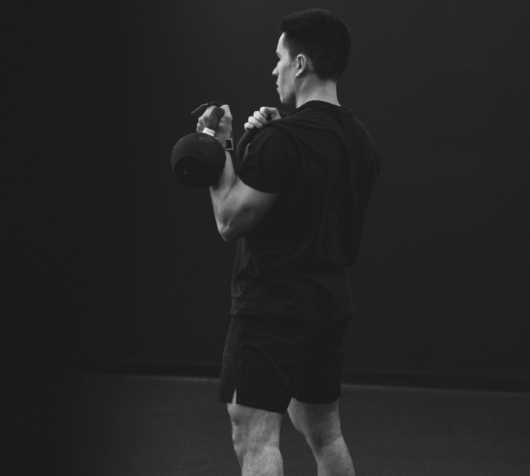 Athlete performing slow, controlled kettlebell presses in a dark gym, focused on posture and range of motion, with no vest.