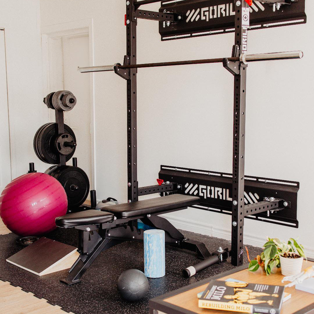 Home gym setup featuring a Gorila power rack, adjustable bench, barbell, and weight plates in a modern living space, showcasing durable Canadian-made fitness equipment.