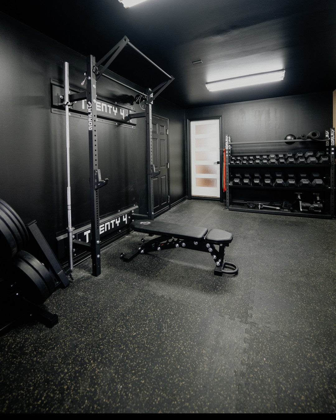Home gym setup featuring a Gorila wallmount rack, adjustable bench, barbell, and weight plates in a modern living space, showcasing durable Canadian-made fitness equipment.