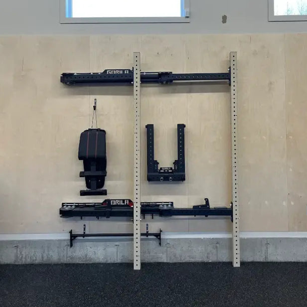 Gorila Fitness AF35 Folding Squat Rack in Tan, Wall-mounted with gym equipment against a beige wall.