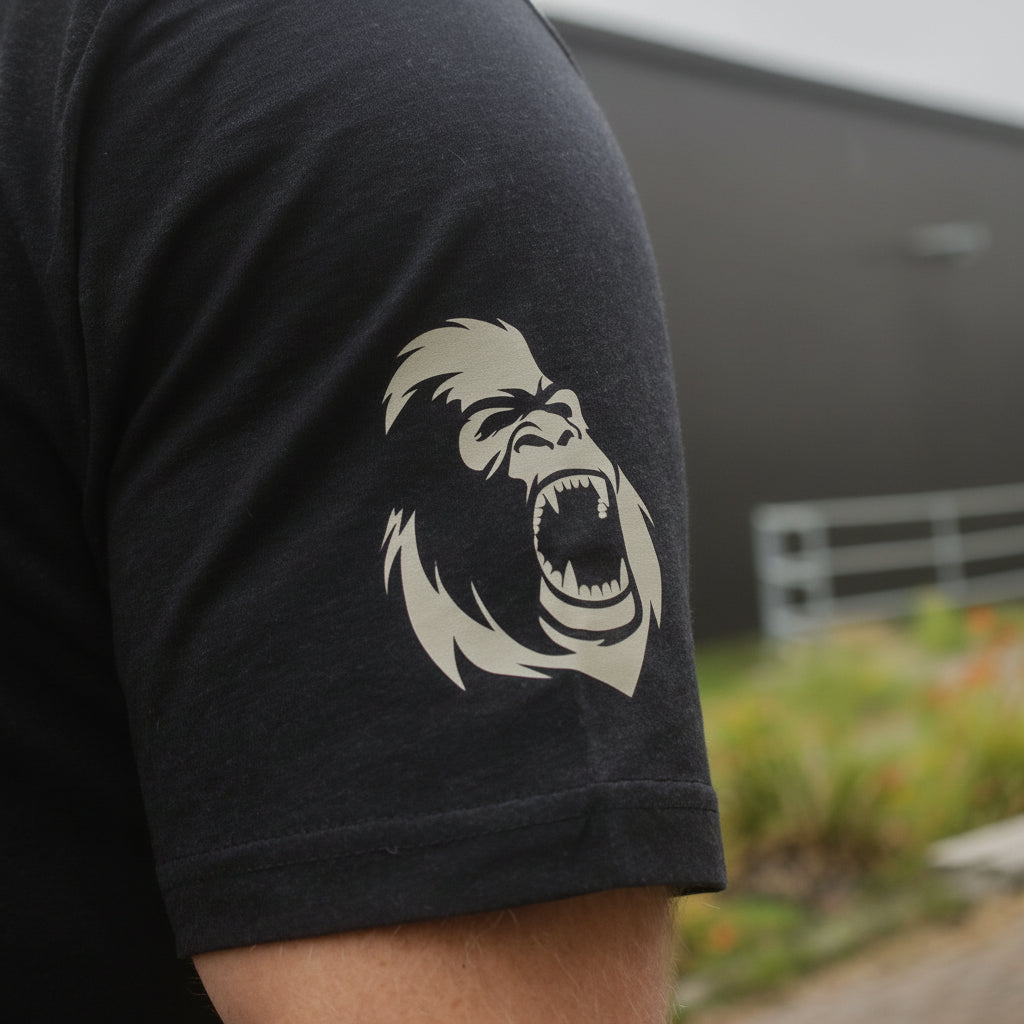 Person wearing a black t-shirt with a tan gorilla graphic on the shoulder, blurred background - Gorila Fitness