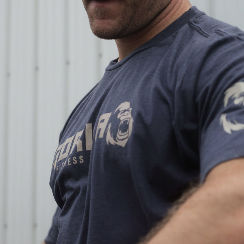 Man wearing a navy blue Gorila Fitness t-shirt with a tan logo, standing against a plain background