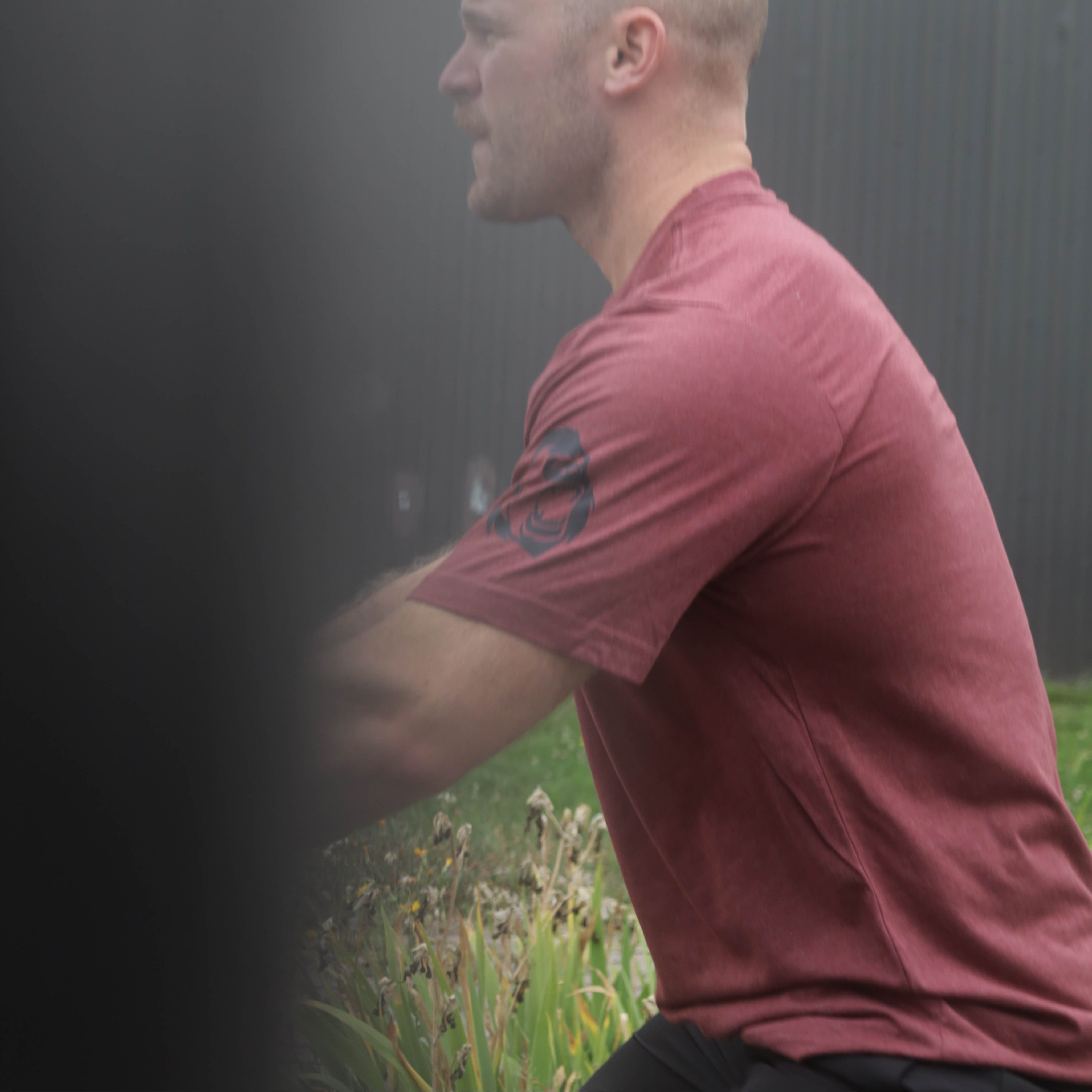 Man in a red shirt standing in a foggy outdoor setting, training outside a Crossfit gym