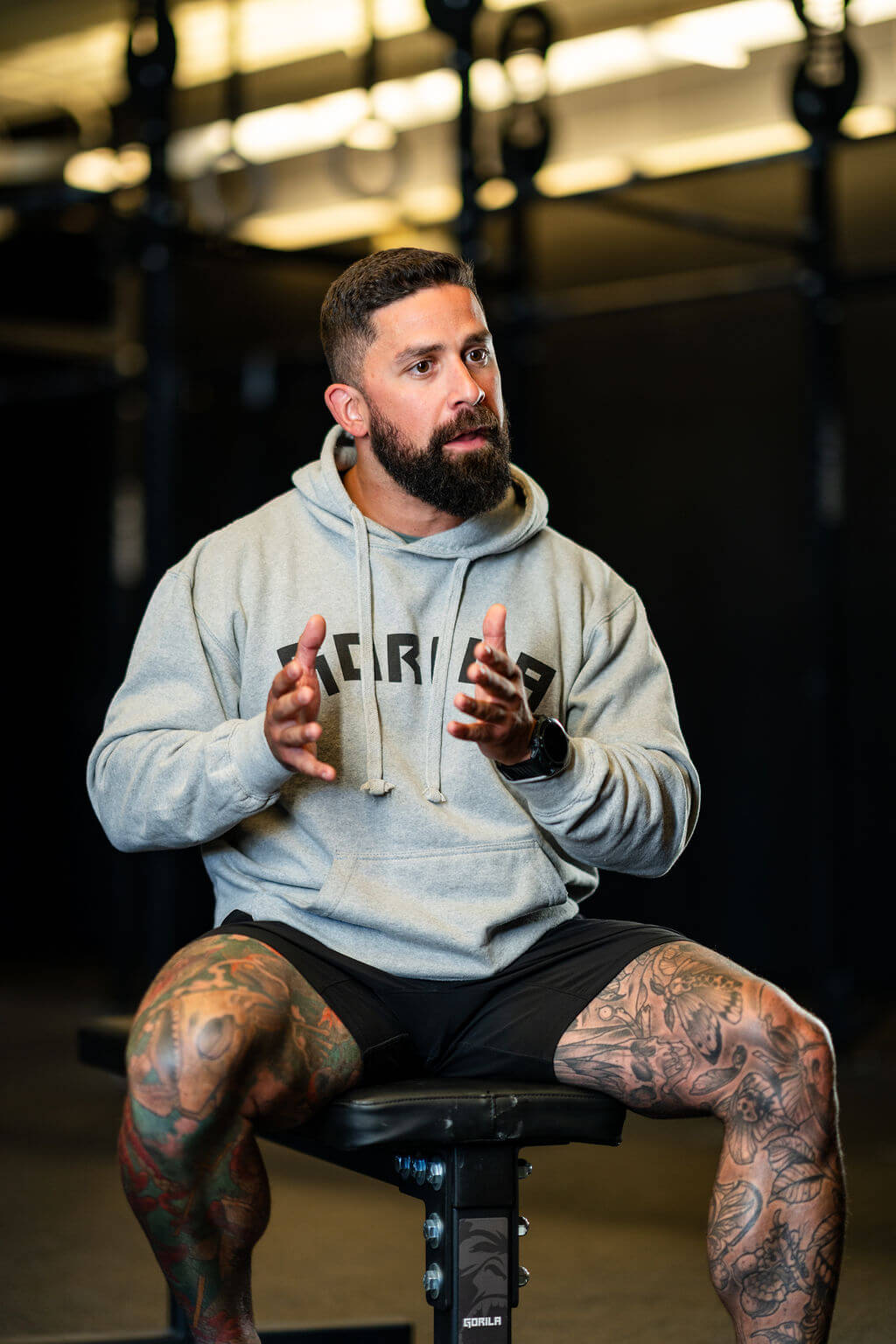 Gorila Gym Project Specialist with tattoos sitting on a stool in a gym setting