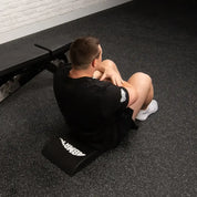 Person using a black exercise abmat on a gym floor with a white brick wall in the background.