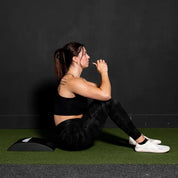 Woman sitting on a black abmat abs trainer against a dark wall