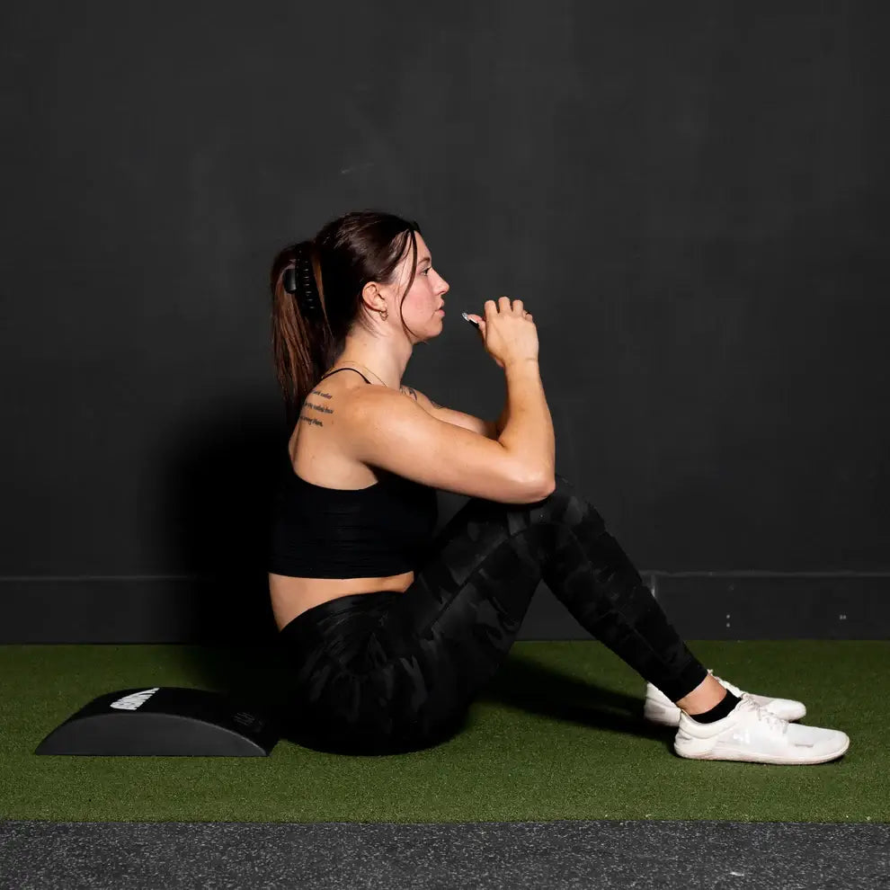 Woman sitting on a black abmat abs trainer against a dark wall