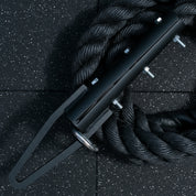 Close-up of the Gorila Blackline Climbing Rope hook resting on black rubber gym flooring, showing the matte finish and heavy-duty steel connector.