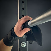Hand wearing a black wrist wrap pull-up grip, cleaning a pull-up bar in a gym setting before a workout