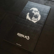 Top view of Gorila Fitness Dollamur training mat in matte black with large roaring gorilla logo and white Gorila branding, designed for strength and conditioning floors.