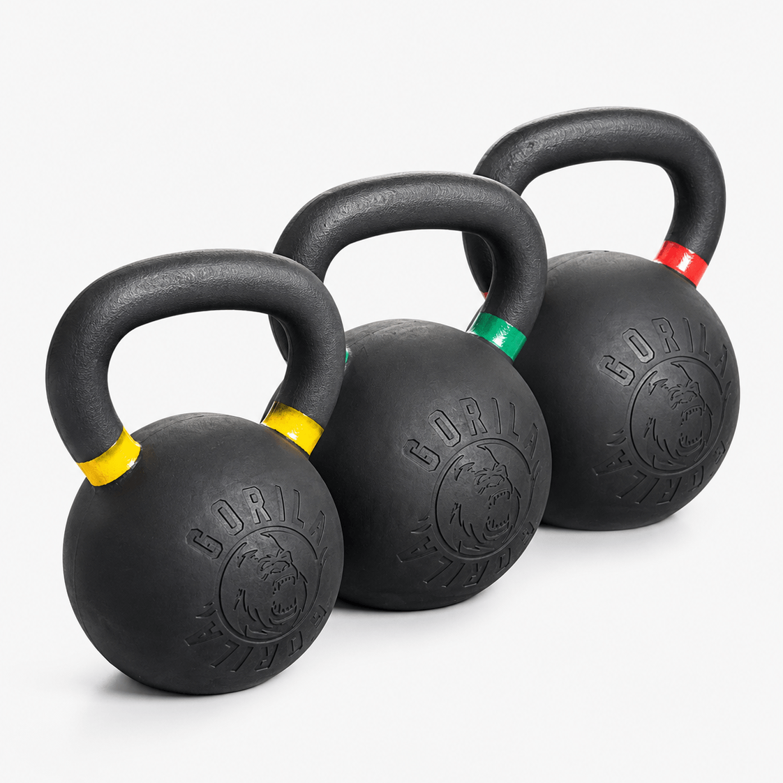 Three black kettlebells with colored bands in yellow, green, and red, arranged diagonally on a light gray background. The kettlebells feature the Gorila Fitness logo embossed.
