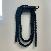 Gorila Rope Storage mounted on a wall with a coiled battle rope hanging from the hook, highlighting its dual-use design for rope and gear storage.