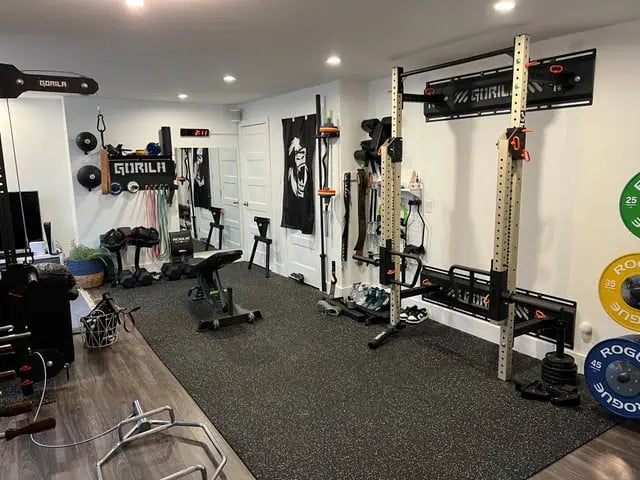 Ultimate Basement Gym with Customizable Rig and Cardio Equipment - This home gym setup features a premium Gorila Fitness squat rack with multiple attachments, wall-mounted storage solutions, and a sleek flooring design. Complete with cardio equipment, dumbbells, and a clean aesthetic, this space maximizes functionality and style for an all-in-one workout experience in your basement. Perfect for anyone looking to bring the gym-quality feel to their own home with high-quality, versatile fitness equipment.